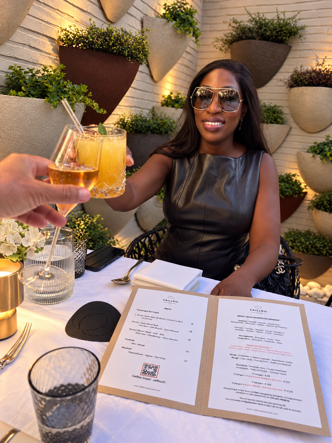 Vanessa in a black dress raising an aperitif at Caillou restaurant in Knokke